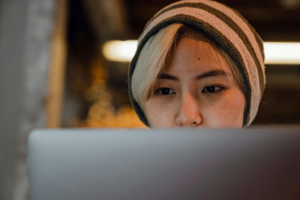 Young woman with beanie concentrating on laptop in cozy café setting.