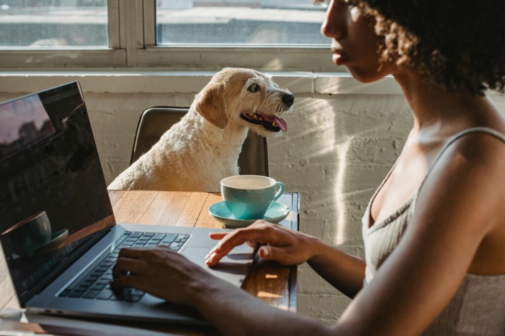 A young woman works remotely at home, accompanied by her loyal dog and a cup of coffee.
